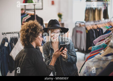 Tausendjährige weibliche Freunde auf der Suche nach einem Smartphone in einem vintage Clothing Store Stockfoto