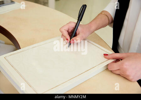 Die Hand des Mädchens hält einen Stift auf ein leeres Blatt Papier. Stockfoto