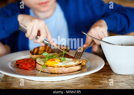 Junge essen Spiegelei auf Toast und Porridge zum Frühstück Stockfoto