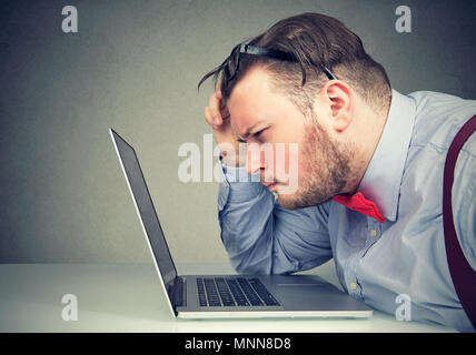 Nahaufnahme der Geschäftsmann aus seiner Brille mit sehstärke Probleme mit Laptop Software auf grauem Hintergrund isoliert verwirrt. Vision die Chan Stockfoto