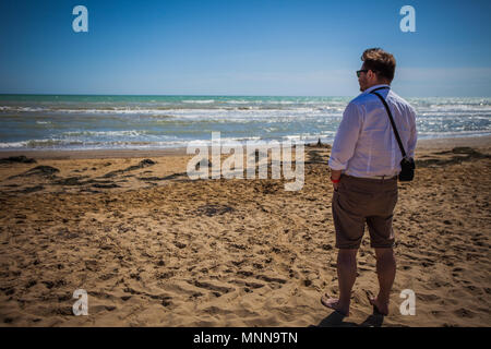 Mann am Strand beobachten die Wellen des Meeres in einem windigen Morgen, Bibione, Venedig, Italien Stockfoto