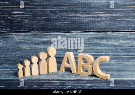 Hölzerne Figuren der Kinder stehen in einer Reihe von klein bis groß in der Nähe der Buchstaben des englischen Alphabets abc. Der Begriff der Bildung und Studium, eine scho Stockfoto