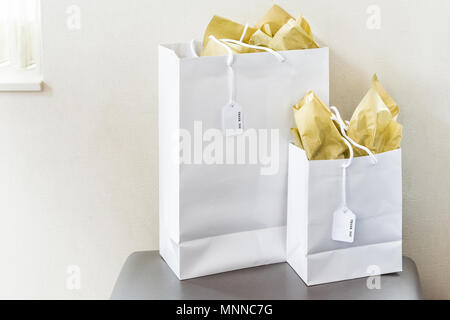 Zwei große Tüten mit vielen Dank Hinweis text Tags auf Stuhl Tisch im Zimmer isoliert, goldgelb Geschenkpapier durch Fenster Wand closeup Stockfoto