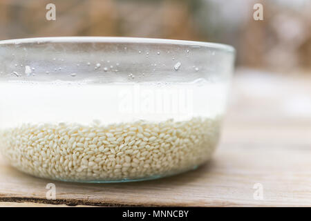 Makro Nahaufnahme des eingeweichten Reis Korn, trübe Flüssigkeit Wasser in Glasschale außerhalb auf hölzernen Deck Stockfoto