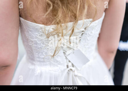 Nahaufnahme zurück der jungen Frau, die versucht, auf geschnürten Korsett Hochzeit Kleid in Boutique Discounter mit Schnürung Ribbon, blondes Haar, Preis Stockfoto