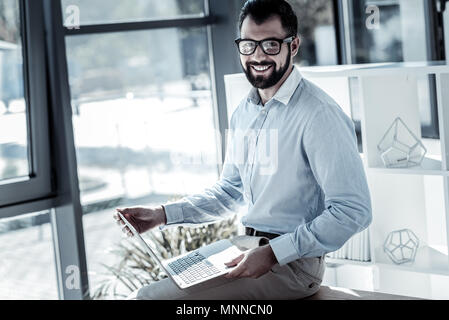 Freudige qualifizierte Arbeitnehmer, die den Laptop und lächelnd. Stockfoto