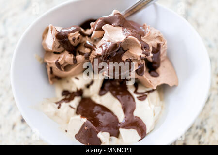 Weiche Vanille- und Schokoladeneis mit dunkelbrauner Sirup Sauce beträufelt closeup in Weiß Schüssel mit Löffel servieren Stockfoto
