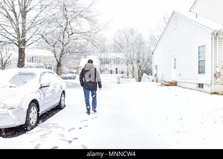 Junger Mann zu Fuß Mit dem Auto in der Einfahrt in Nachbarschaft mit Schnee Boden während Blizzard weiße Sturm abgedeckt, Schneeflocken in Virginia Vororten fallen, sin Stockfoto