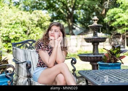 Junge Frau sitzt auf der Terrasse im freien Stuhl im Frühling Garten im Hinterhof Halle home Glücklich lächelnde Zen mit Springbrunnen, Tisch, Pflanzen