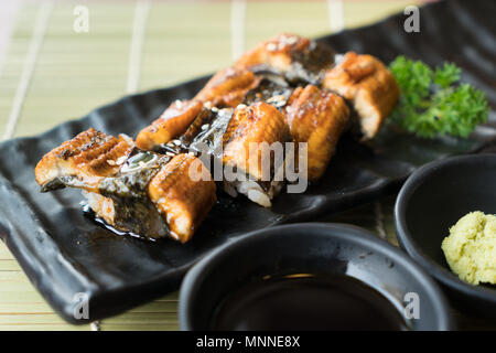 Unagi Sushi auf schwarze Platte zusammen mit japanischen Sauce und green leaf Dekoration, Japanisches Essen, Sushi zu schließen. Stockfoto