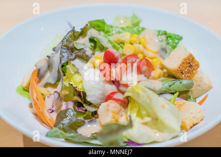 Frischer Salat mit Hähnchen, Tomaten und gemischter Salat (Rucola, mesclun, papiermache) in Weiß Schüssel auf Holztisch. Gesundes Essen. Stockfoto