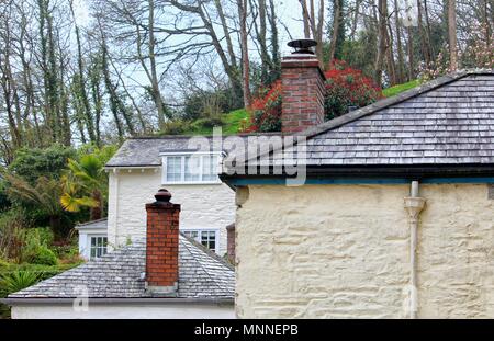 Old Red Brick Schornsteine auf schiefer überdachte Gebäude, mit Pflanzen und Bäumen im Hintergrund. Stockfoto