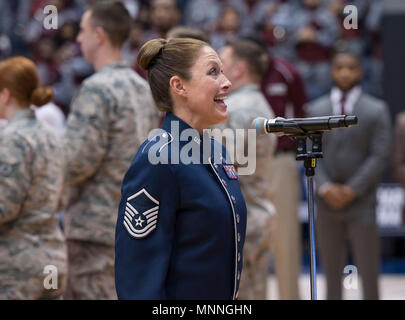 Master Sgt. Alyson Jones, US Air Force Band von Sänger, singt die Nationalhymne als Wright-Patterson Air Force Base, Ohio, Flieger einer großen Garnison - Größe amerikanische Flagge während der pregame Zeremonien halten vor der ersten vier NCAA Turnier an der Universität von Dayton Arena in Dayton, Ohio, 14. März 2018. Während Halbzeit Ereignisse des Spiels, Generalleutnant Robert McMurry jr., Air Force Life Cycle Management Center Commander, den Eid der Rekrutierung zu verspäteter Eintragung Personal verabreicht. Stockfoto