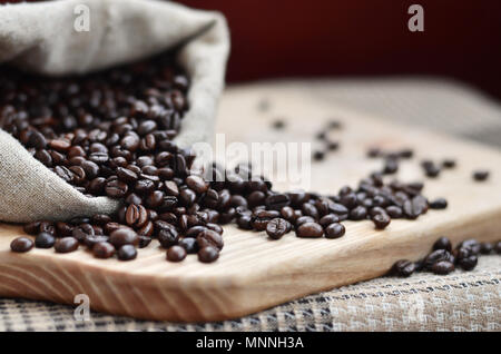 Einen vollen Beutel der braunen Bohnen liegt auf einem Holz- Oberfläche. Attribute, die mit der Zubereitung von Kaffee im Zusammenhang Stockfoto