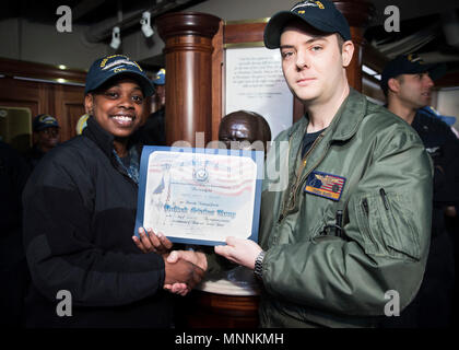 NORFOLK, Virginia (Mar. 16, 2018) - der Luftfahrt Bootsmann Mate (Ausrüstung) Airman Abriel Thomas, von Groesback, Texas, zu USS Gerald R. Ford's (CVN 78) Luft Abteilung zugewiesen, erhält ein Zertifikat, das der Entlastung von Leutnant Adam Boyd während Ihrer reenlistment Zeremonie. Stockfoto