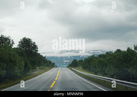 Blick auf die Straße mit niedrig hängenden Wolken und ein Gebirge im Hintergrund. Stockfoto