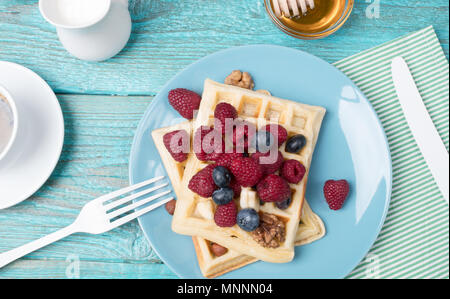 Selbstgemachte Waffeln mit Himbeeren und Blaubeeren, Tasse Kaffee, Milch und Besteck Stockfoto