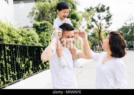 Cute Asian Vater huckepack sein Sohn zusammen mit seiner Frau im Park. Aufgeregt Familie Zeit miteinander zu verbringen mit Glück Stockfoto