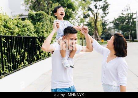 Cute Asian Vater huckepack sein Sohn zusammen mit seiner Frau im Park. Familie begeistert die Hände zusammen mit Glück Stockfoto