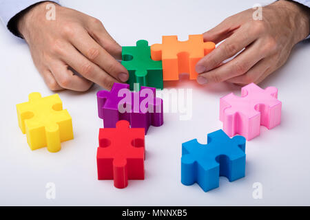 Einer Person Hand lösen Bunte Puzzle auf weißem Hintergrund Stockfoto