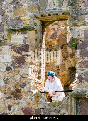 Dirleton, East Lothian, Schottland, UK, 19. Mai 2018. Dirleton Castle Angriff Re-enactment. Die historische Saltire Society staging a tongue-in-cheek Re-enactment eines Angriffs von Robert the Bruce, König von Schottland, um 1311, das Schloss aus dem Englischen, in authentischer Kleidung und Rüstung gekleidet und schwingende replica Waffen im historischen Umfeld Schottland Dirleton Castle. Ein junger Mann im Kostüm auf einer Burg Fenster. Stockfoto