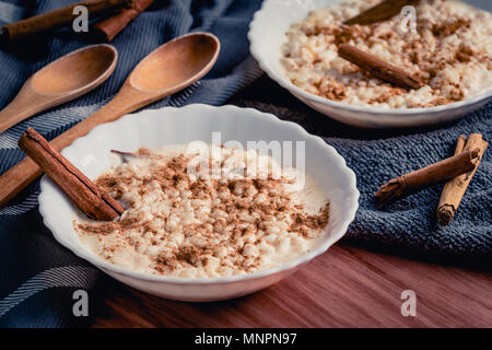 Zusammensetzung der wenigen Keramische Platten mit gekochtem cremiger Milchreis und bestreut mit Pulver und Sticks von Zimt Stockfoto