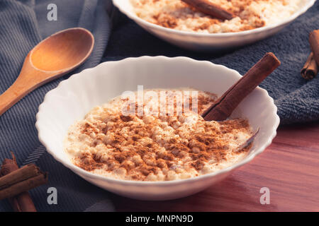 Zusammensetzung der wenigen Keramische Platten mit gekochtem cremiger Milchreis und bestreut mit Pulver und Sticks von Zimt Stockfoto