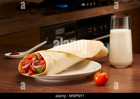 Köstliche shawarma mit Fleisch, Tomaten, Zwiebeln und Petersilie auf weißem Porzellan Teller, Soße und Glas Milch auf Küche aus dunklem Hintergrund. Gerichte o Stockfoto
