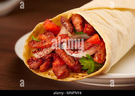 Clouse, köstliche Shawarma mit Fleisch, Tomaten, Zwiebeln und Petersilie auf dunklen Holztisch Hintergrund. Gerichte der orientalischen Küche, Eastern Food. Stockfoto