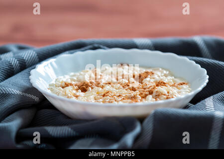 Nahaufnahme der weiße Schüssel mit cremiger Milchreis mit Zimt auf Stoff serviert geerdet Stockfoto