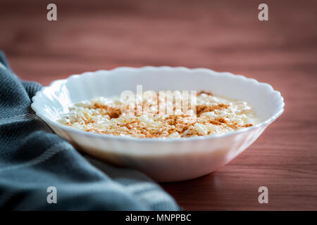 Nahaufnahme der weiße Schüssel mit cremiger Milchreis mit Zimt auf Stoff serviert geerdet Stockfoto