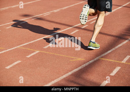 Beine und Schatten eines männlichen Athleten laufen auf der Strecke. Stockfoto