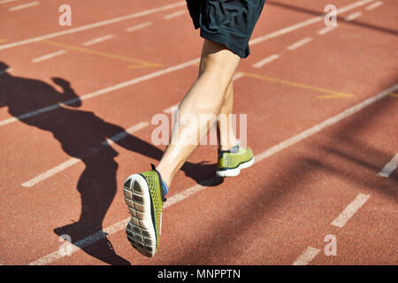 Beine und Schatten eines männlichen Athleten laufen auf der Strecke. Stockfoto