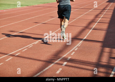 Beine und Schatten eines männlichen Athleten laufen auf der Strecke. Stockfoto