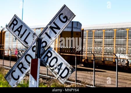 Alte, abgetragene Bahnübergang Zeichen vor einem Stacheldrahtzaun und Autos in den Tag Stockfoto