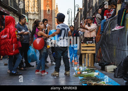 Erwachsene und Kinder versammeln sich um ein traditionelles Arzneimittel pflanzliche Stärkungsmittel Verkäufer tasting Samples, die in der Straße von den Central District, Mexiko City, Mexiko. Stockfoto