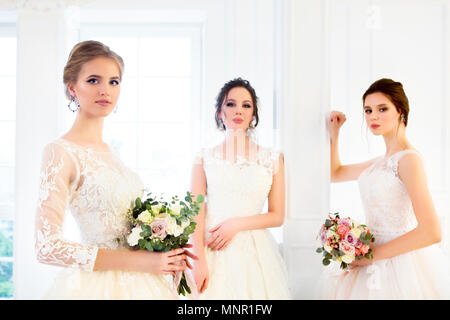 Drei junge Frau mit Blumensträuße tragen Brautkleider Stockfoto