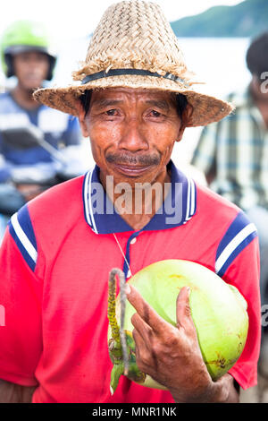 LOMBOK, Indonesien - 11. Februar: arme Mann mit Strohhut Verkauf eine Kokosnuss auf Februar 11,2012 Lombok, Indonesien. Kokosnuss Wasser ist beliebtes Getränk in der Stockfoto