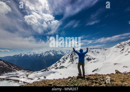 Man steht auf einer Klippe in Snowy Mountains mit hands up Stockfoto