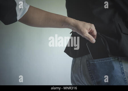 Nahaufnahme einer die Hand der Dieb Diebstahl der Geldbörse zu einer Frau. Dieb Diebstahl Geldbörse aus der Tasche auf der Rückseite einer Frau. Stockfoto