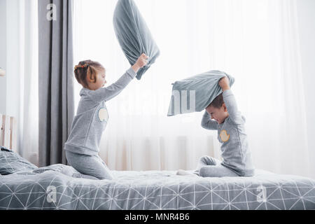 Kleine Jungen und Mädchen inszenierten eine Kissenschlacht auf dem Bett im Schlafzimmer. Freche Kinder schlagen einander Kissen. Sie mögen diese Art von Spiel Stockfoto