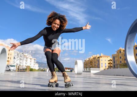 Junge passen schwarze Frau auf Rollschuhen reiten im Freien auf Urban Street mit offenen Armen. Lächelnde Mädchen mit Afro Frisur rollerblading an einem sonnigen Tag Stockfoto