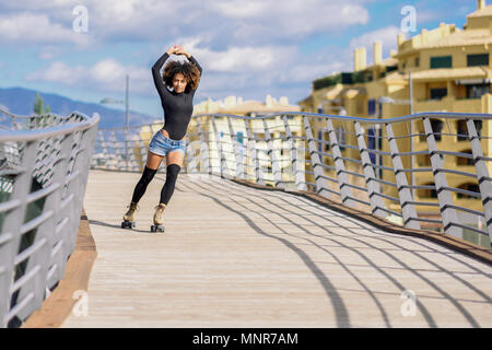 Junge passen schwarze Frau auf Rollschuhen reiten im Freien auf städtischen Brücke mit offenen Armen. Lächelnde Mädchen mit Afro Frisur rollerblading an einem sonnigen Tag. Werden Stockfoto