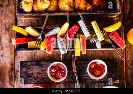 Blick von oben auf die leckeren Bio essen zum Frühstück auf rustikalen Holztisch. Obst, Saft, Croissants und Marmelade flach. Stockfoto