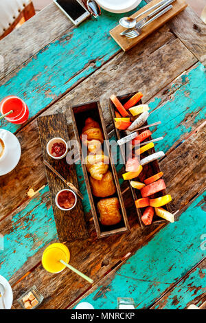 Blick von oben auf die leckeren Bio essen zum Frühstück auf rustikalen Holztisch. Kaffee, Eier, Obst, Saft, Croissants und Marmelade. Stockfoto