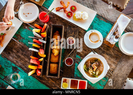 Blick von oben auf die leckeren Bio essen zum Frühstück auf rustikalen Holztisch. Kaffee, Eier, Obst, Saft, Croissants und Marmelade. Stockfoto
