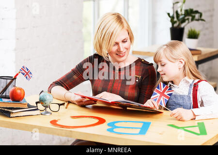 Elegante englische Erzieher Studieren mit Kind Mädchen, lesen Buch auf dem Tisch mit Buchstaben, Sprache kind Lernprozess in weißen, eleganten Klassenzimmer Stockfoto