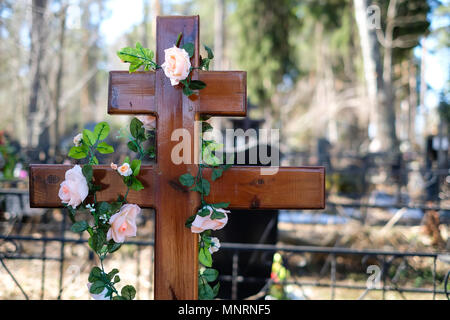 Künstliche Blumen Girlande oder Kranz von Rosen auf das Kreuz auf dem Grab im Frühjahr. Friedhof Dekorationen. Selektive konzentrieren. Stockfoto