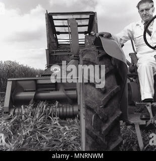 1960, historische Bild eines männlichen Landwirt auf seinem Traktor die Ernte einer Ernte von Weizen. In dieser Zeit, viele Landwirte dazu verwendet wird, Traktor montiert Erntegut Erntemaschinen, England, UK. Stockfoto