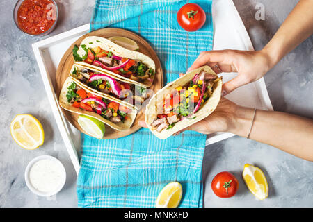 Weibliche Hände halten mexikanische Tacos Schweinefleisch mit Gemüse. Tacos al Pastor auf Holz blau im Hintergrund. Ansicht von oben Stockfoto